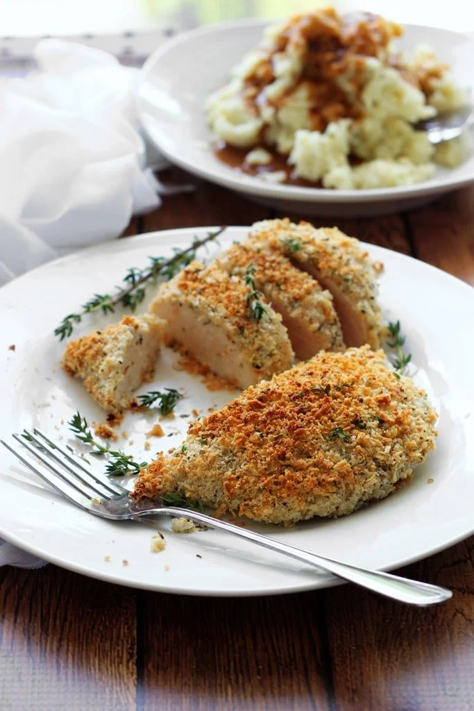 Baked Parmesan Herb Crusted Chicken on a colorful plate with herbs