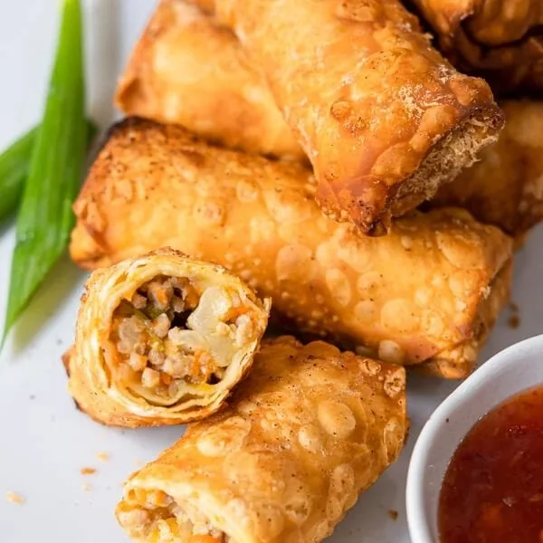 Plate of crispy chicken egg rolls served with dipping sauce.