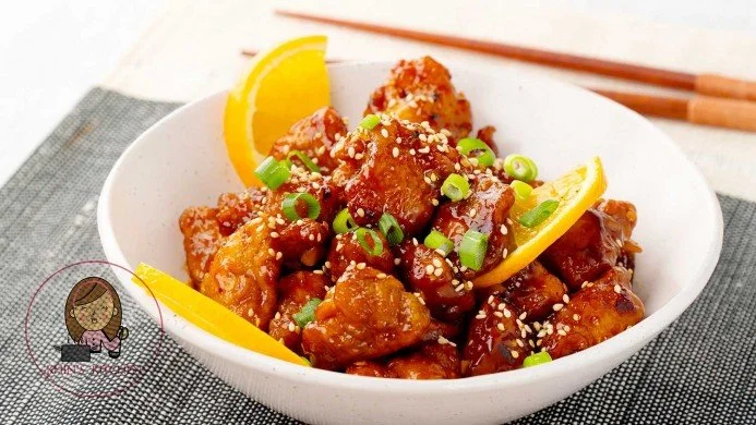 Plate of crispy orange chicken garnished with green onions and sesame seeds