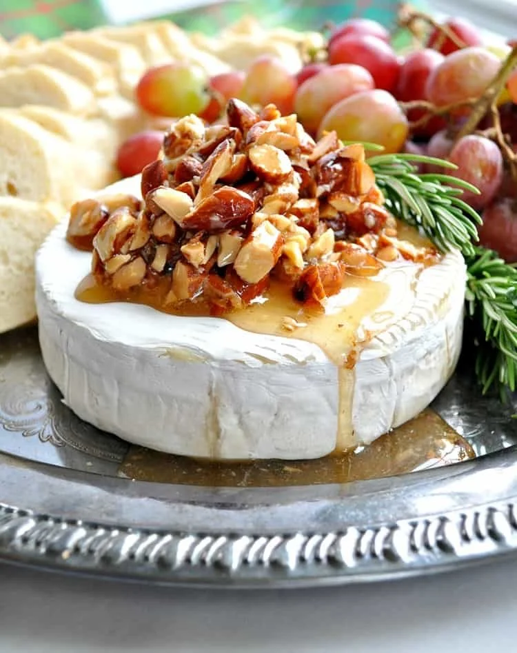 Honey Glazed Almond Brie topped with honey and almonds on a wooden board