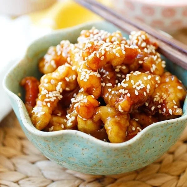 Plate of flavorful sesame chicken garnished with sesame seeds and vegetables