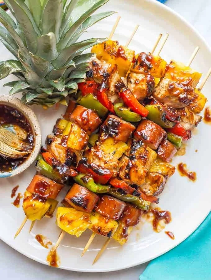 Teriyaki chicken pineapple skewers garnished with fresh herbs on a grill.